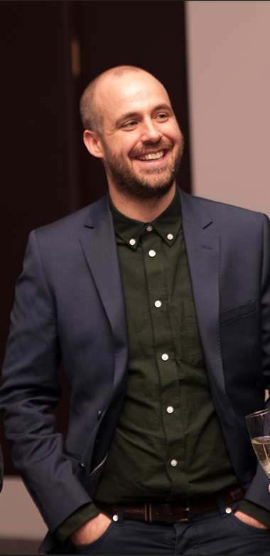 man standing with hands in pocket smiling